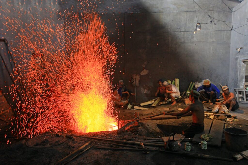 Industrial setting with workers forging metal, surrounded by vibrant sparks.